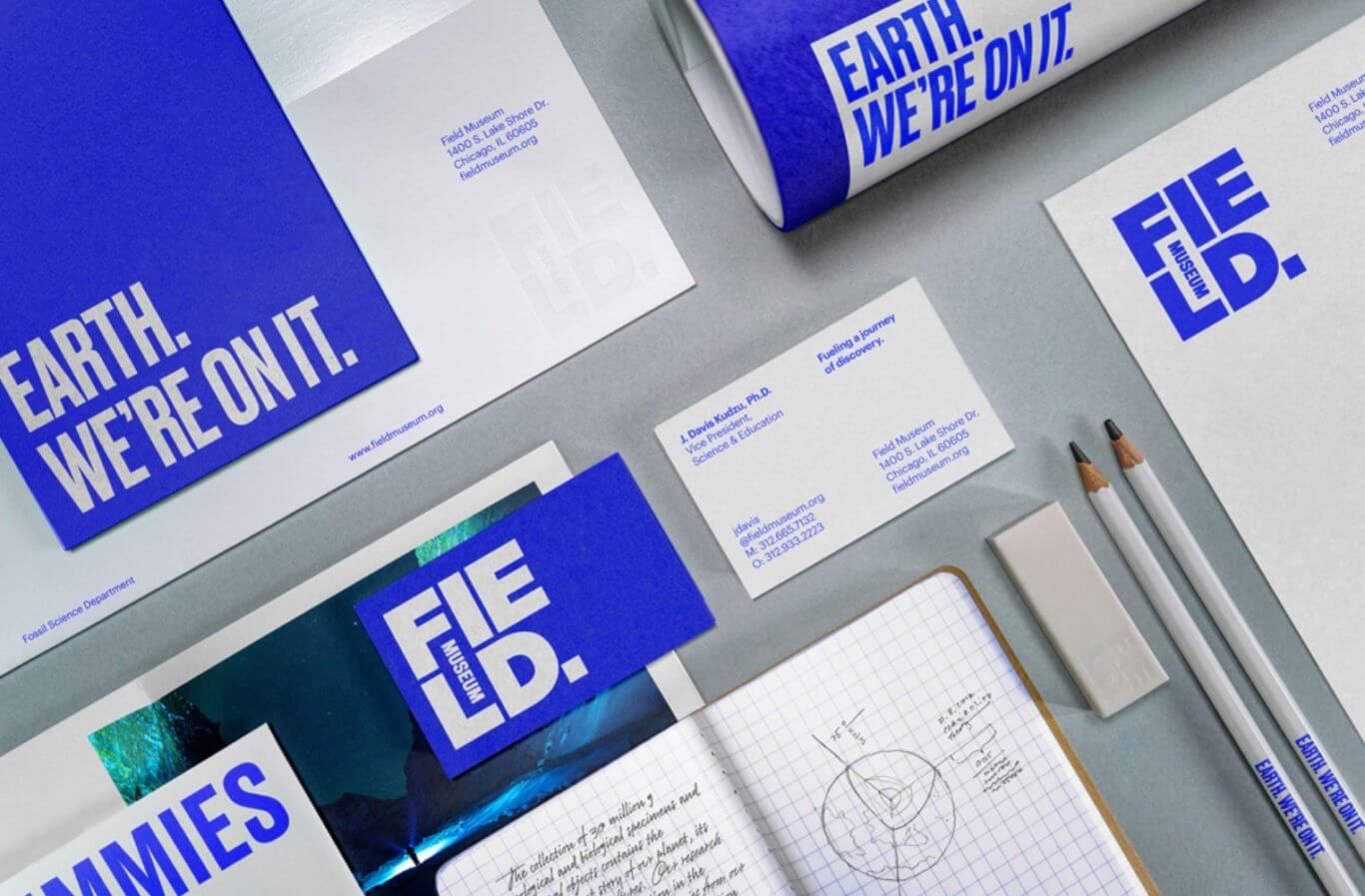 Bright blue and white Field Museum–branded business cards, notecards, pencils, and letterhead are neatly laid out on top of a grey surface.