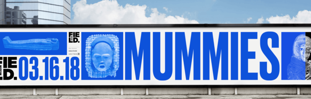 A Field Museum billboard rendered almost entirely in blue with the a large text reading "MUMMIES" accompanied by images of a skeleton, sarcophagi, a mask, and exhibition dates.