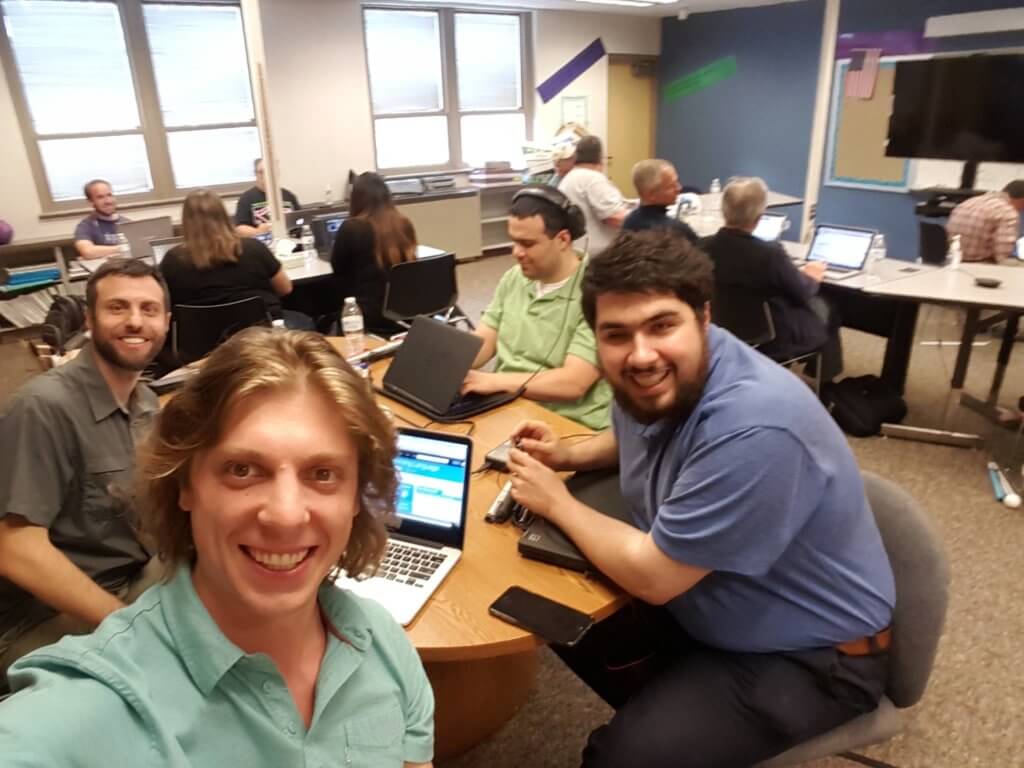 A selfie of Sina and three other people all smiling broadly with laptops sitting at a round table in a computer lab.